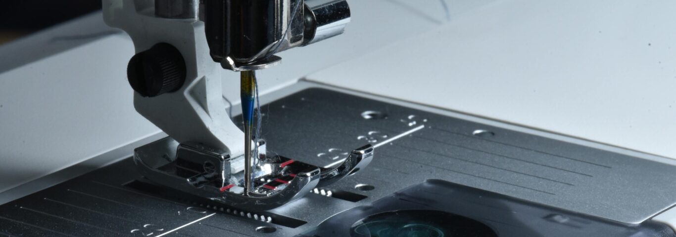 Detailed view of a sewing machine needle and presser foot on a sewing machine.